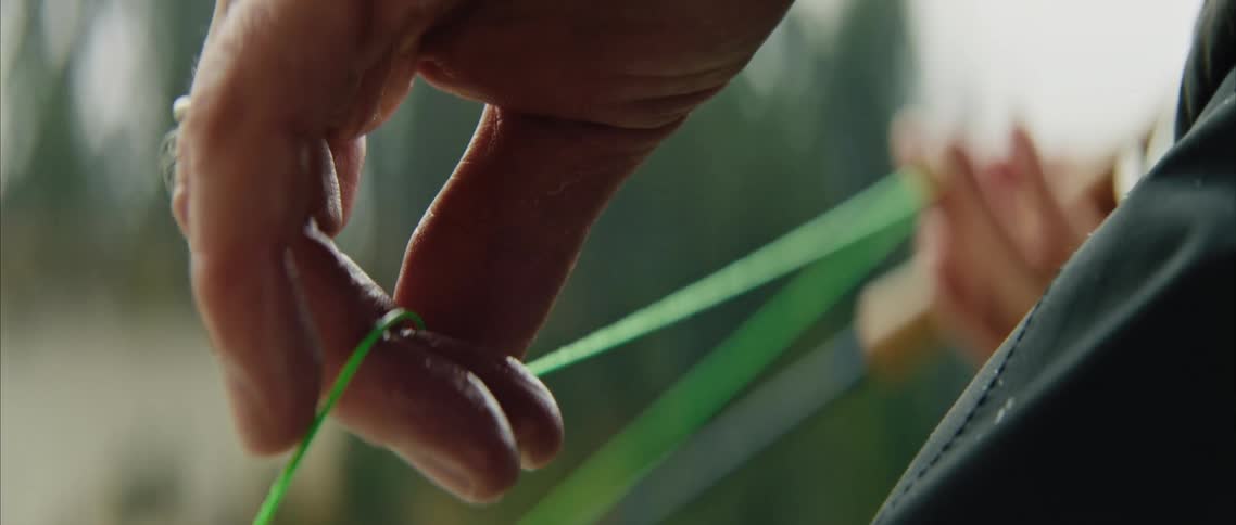 Close up of the hand of a man slowly pulling a green line on a fishing rod under the rain