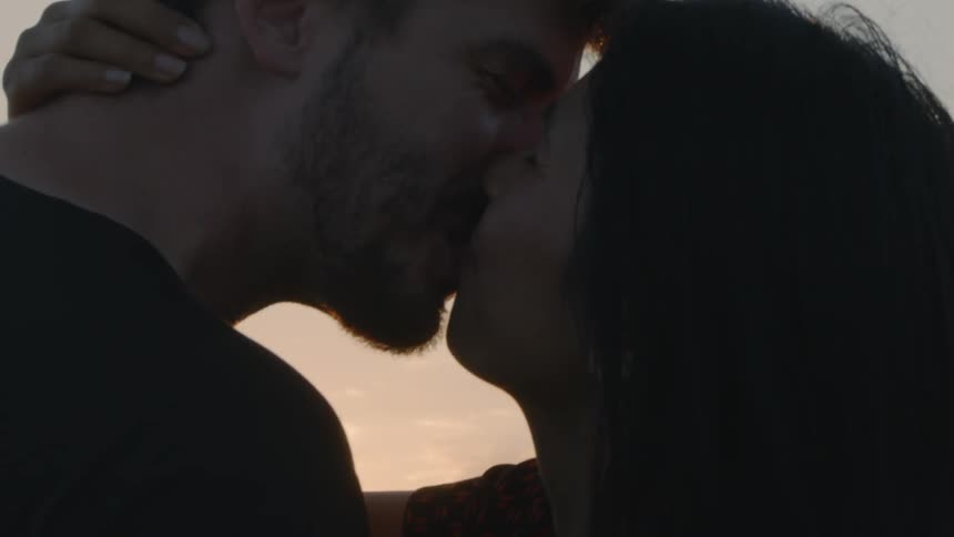 Woman with straight black hair makes out with man with beard and black sweater laughing at dusk