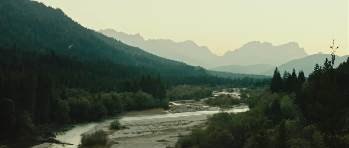 View of river with long line across land next to mountain forest at dawn