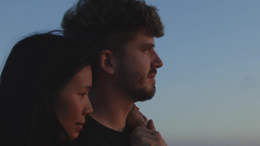 A man and woman hugging and close while they stand outside at sunset