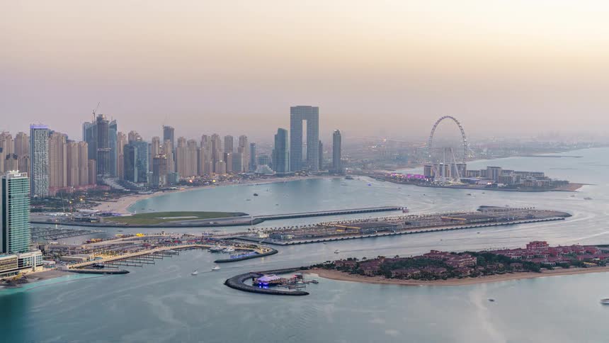 Skyline of the futuristic metropolitan city of dubai as boats sail in the water and day turns to night and the city lights up