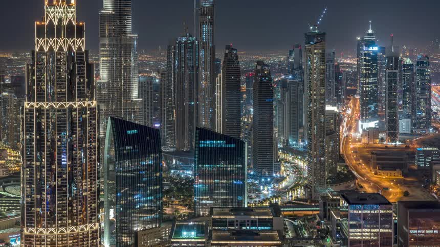 Traffic flows along busy highways through city and passes skyscraper under construction at night