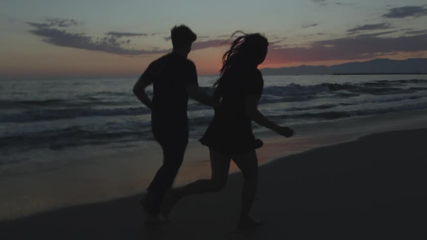 A couple hold hands while running on the beach