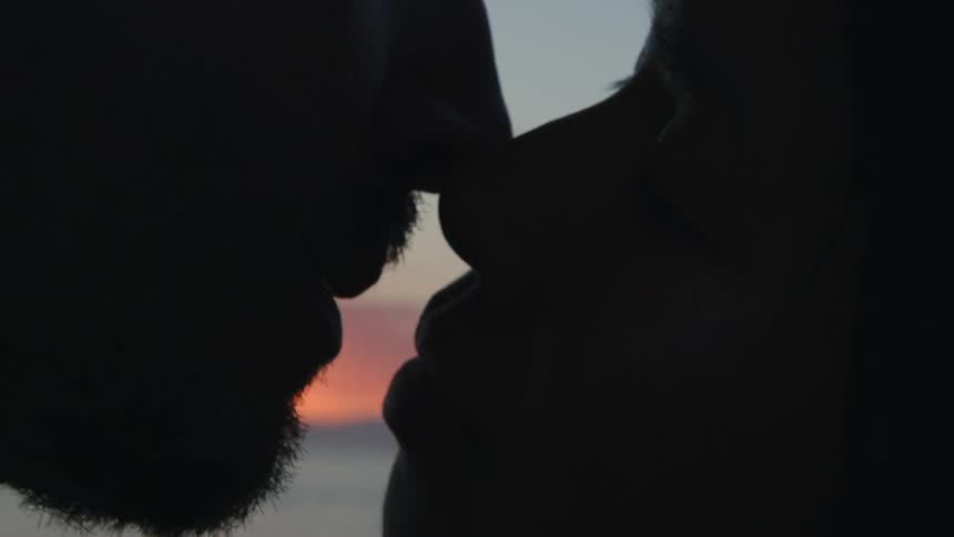 The silhouette of a couple kissing and smiling as they separate at the beach at sunset