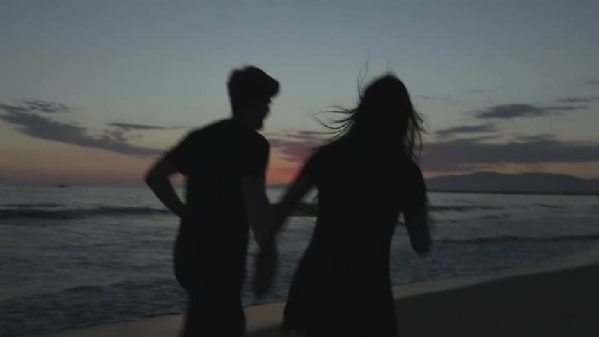 A woman and man are holding hands as they run along a beach