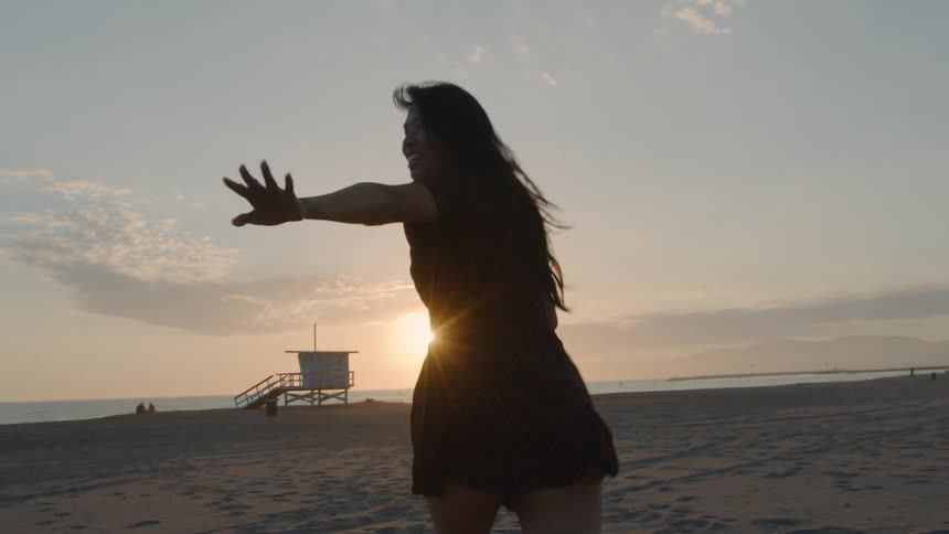 A woman runs across a beach while gesturing towards a person out of frame