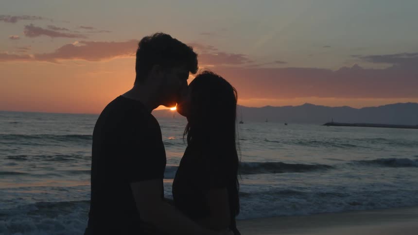 The silhouette of two people standing on the beach kissing at sunset