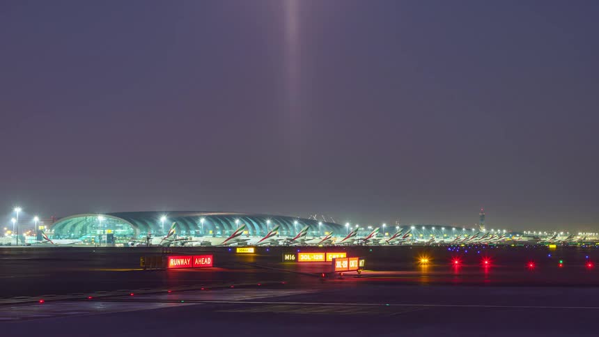 Airplanes travel along a runway at a large airport at night