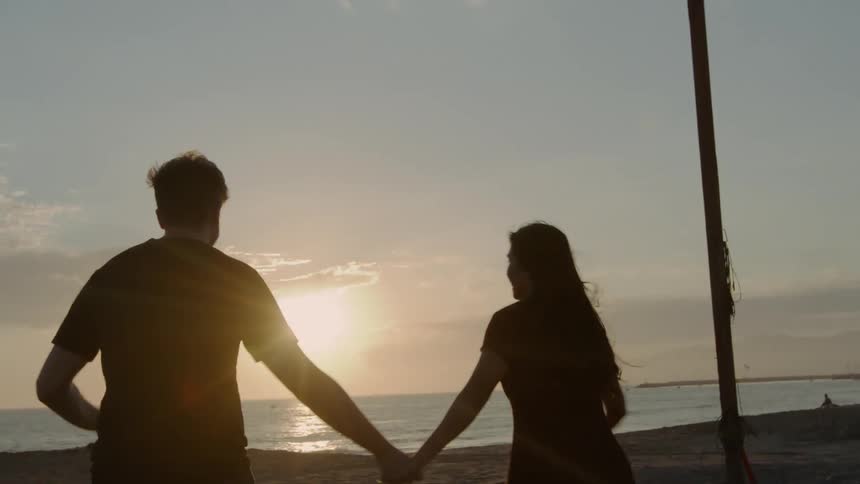 A couple hold hands as they run toward the ocean