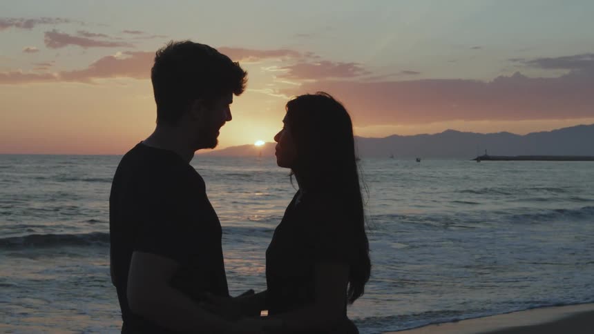 A couple face each other as they hold hands on the beach