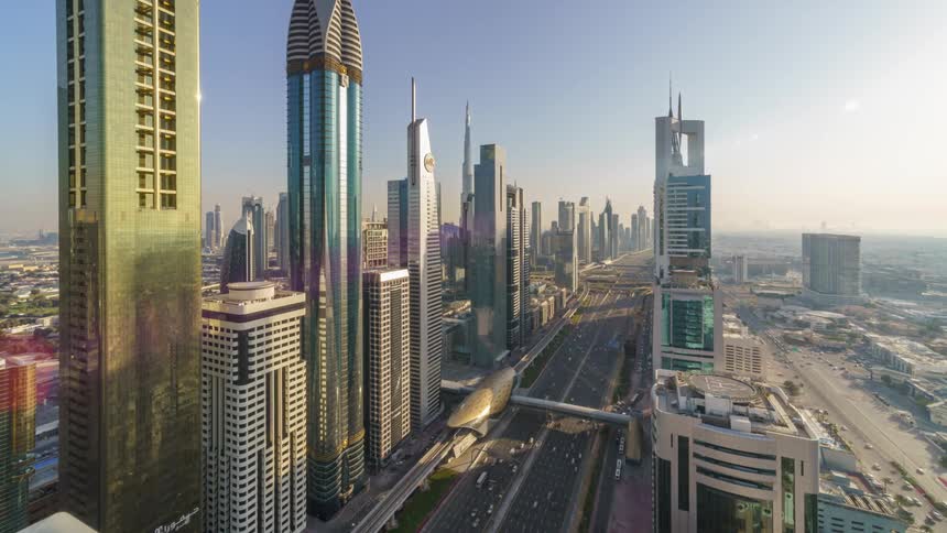 The dubai city skyscrapers and buildings with cars traveling on busy streets and train station glowing golden