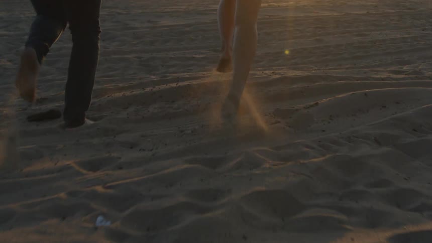 Woman wearing black skirt and man with black pants run on the beach at sunset