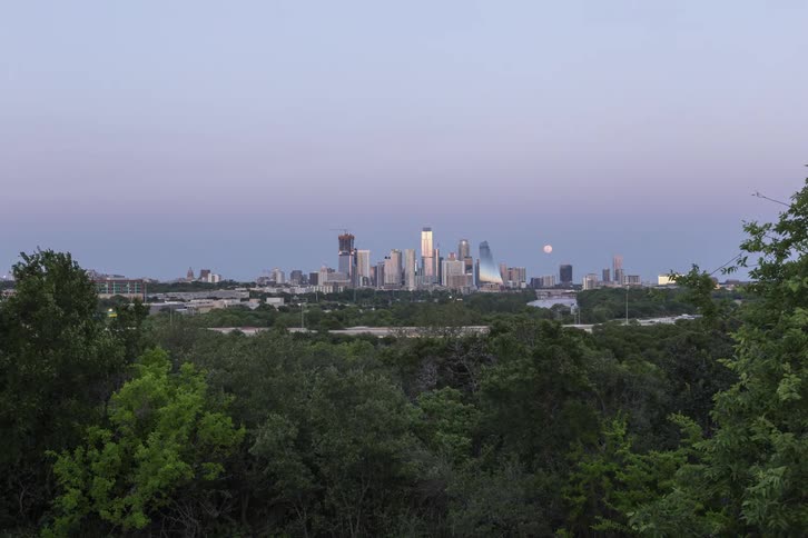 Traffic passes between woods and near city downtown
