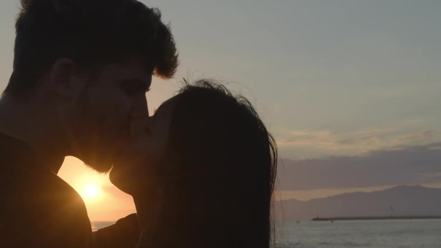 Silhouette of a young couple kissing at sunset next to the ocean