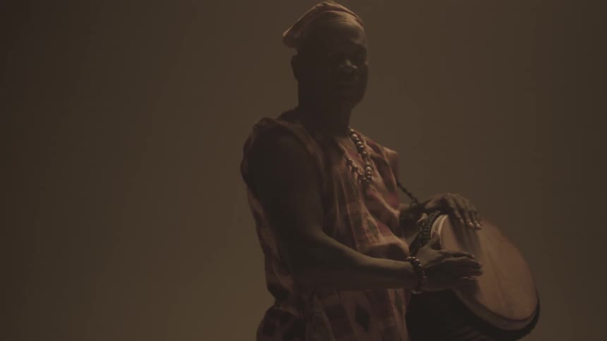 Man standing in dim room holding a bongo drum