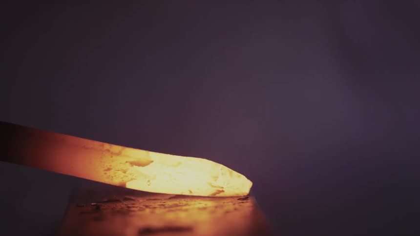 A person is hammering hot metal on a slab