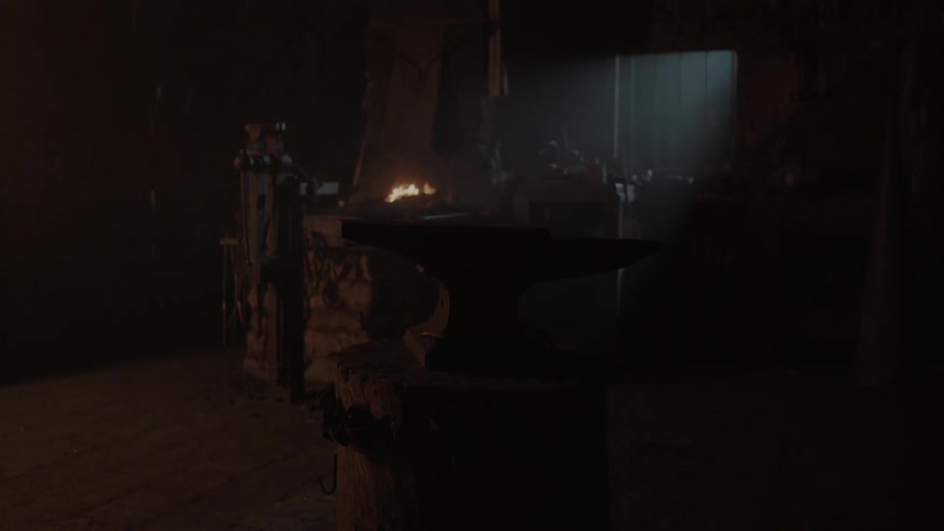 A blacksmith has a fire going in a dark room