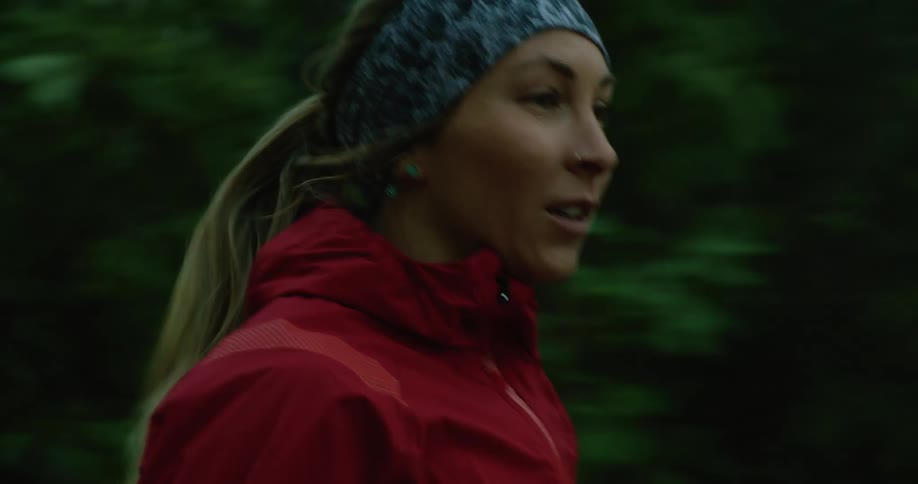 Young woman wearing a red jacket jogs near a forest covered in mist at morning