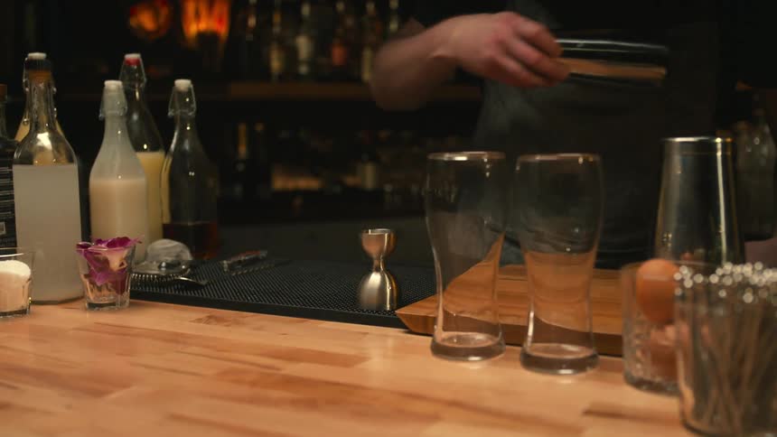 Bartender puts metal drink shakers on bar surface in preparation to mix a drink