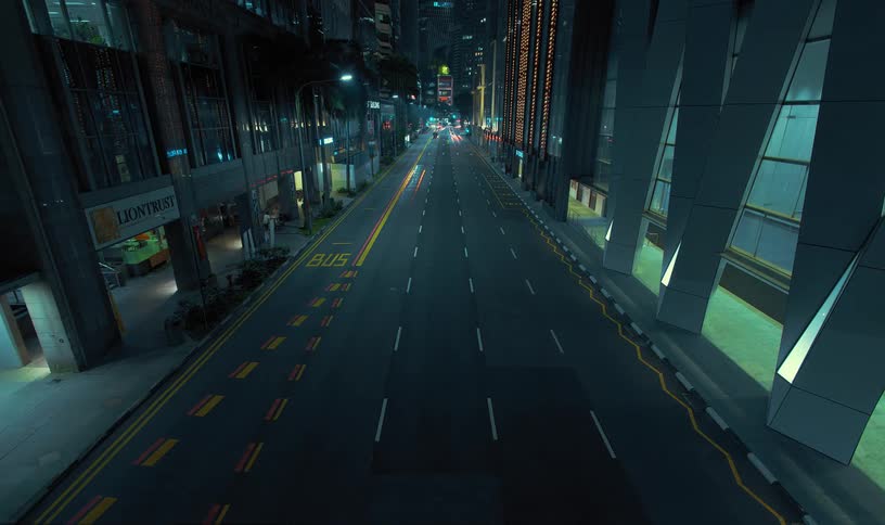 Lights on vehicles shine as they travel on a road between dimly lit downtown buildings