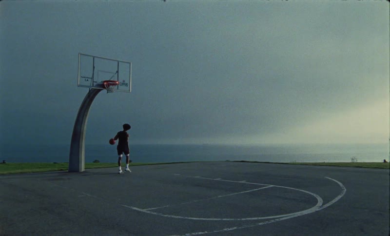 A man performs a flashy slam dunk on an outdoor basketball court on a cloudy day