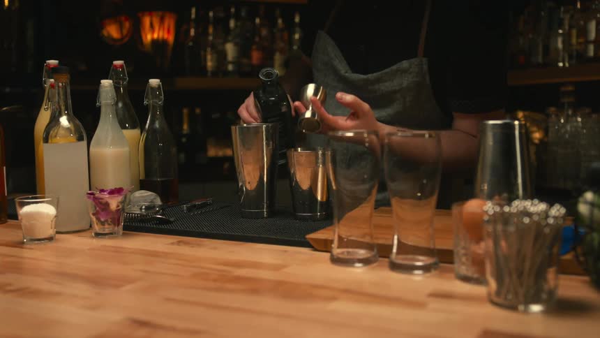 A bartender pours alcohol into a jigger before dumping jigger into a cocktail shaker