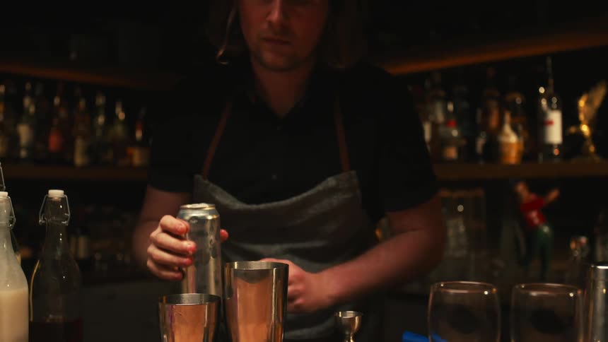 A bartender pours a soda into a cocktail glass
