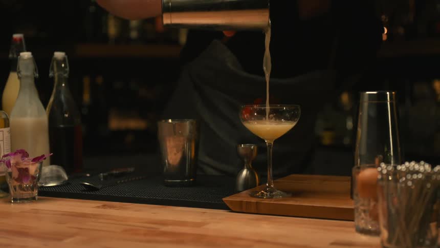 A bartender is pouring a mixed drink from a metal container into a glass