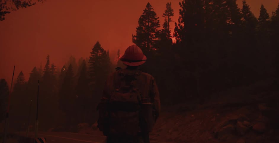A fireman is standing outside of a burning forest as the sky is red