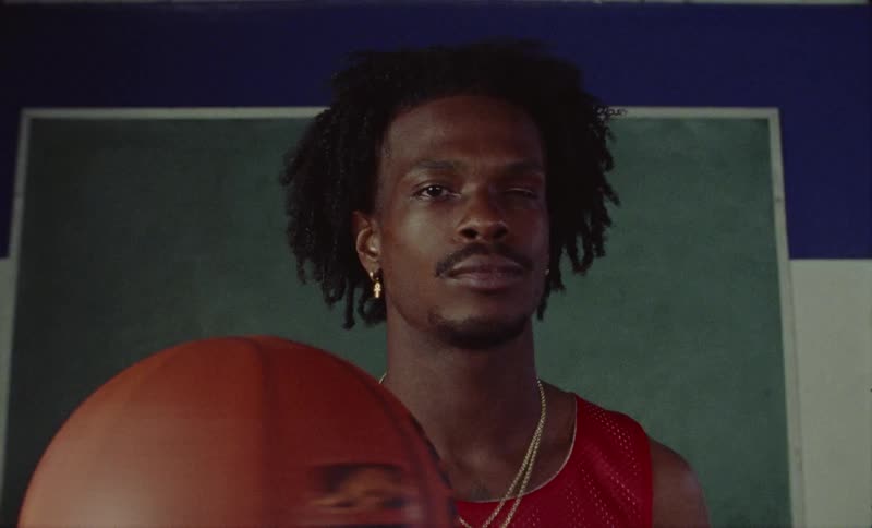 A man is standing in a room spinning a basketball on his hand as lights flash upon him