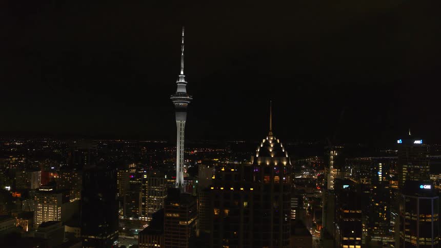 The sky tower standing tall above the auckland skyline with lights glowing at night