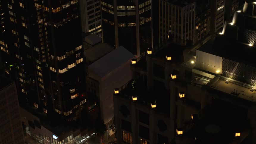 Aerial view of tall inner city buildings lit up at night with cars on the street