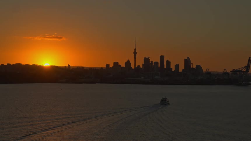 Aerial view of a boat moving on the calm surface of the ocean in front of the city skyline at sunset