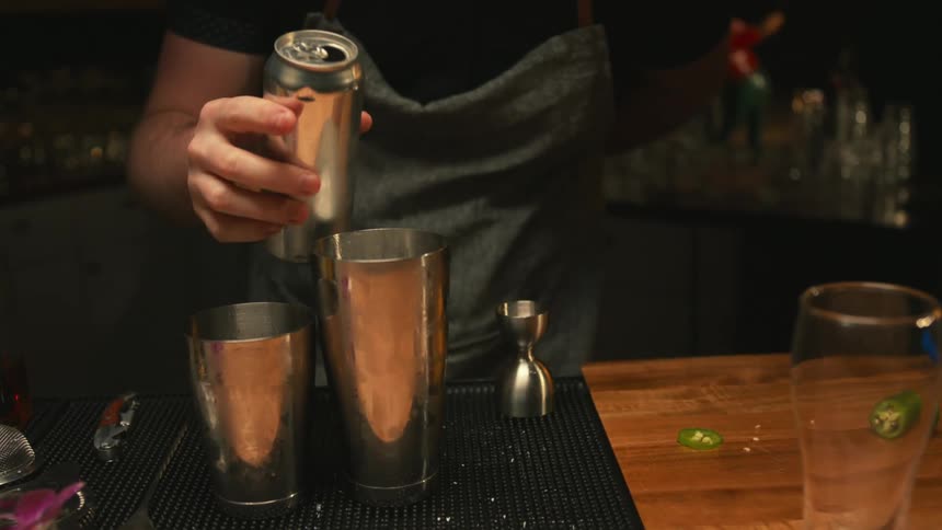 A bartender pours a canned drink into a cocktail shaker