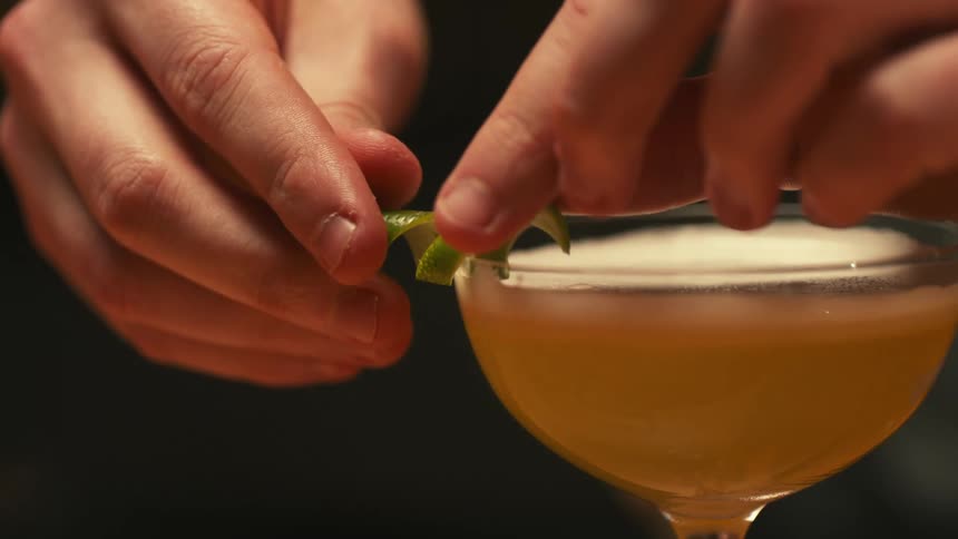 A person places a twist of lime on the rim of a glass with a drink inside