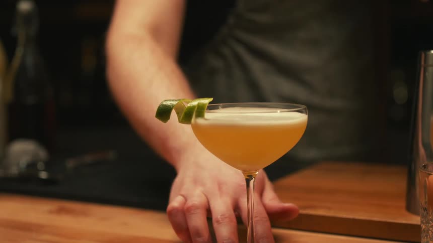 A bartender pushes a cocktail toward the edge of the bar