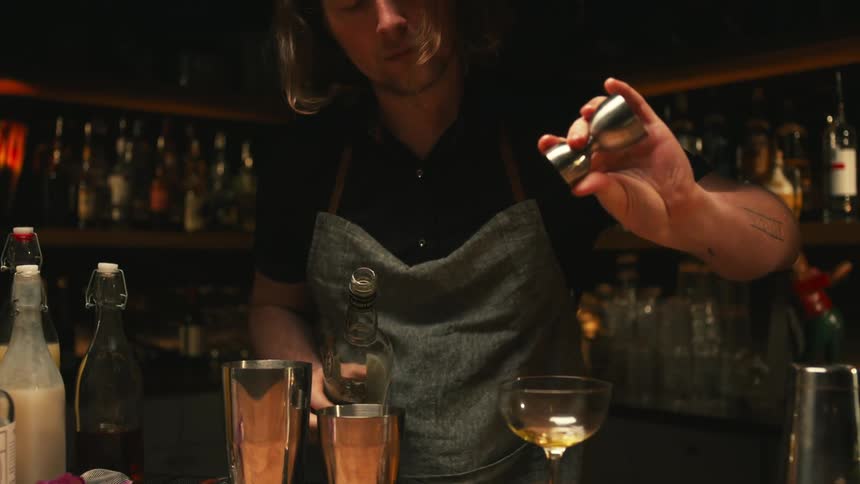 Bartender mixes drink while standing at bar in dim area