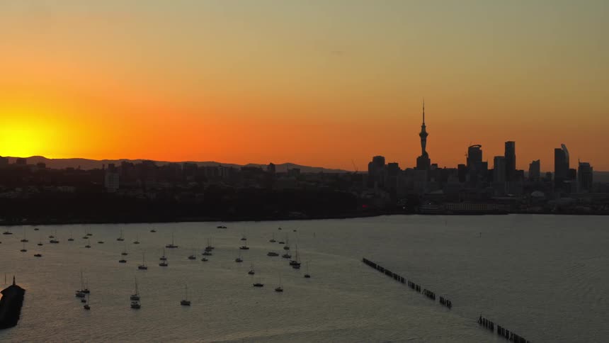 Boats and ships in a marina with the city tower and building silhouette in a golden sky