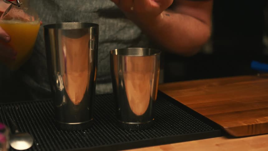 A bartender pours juice in to a shot glass and in to a shaker