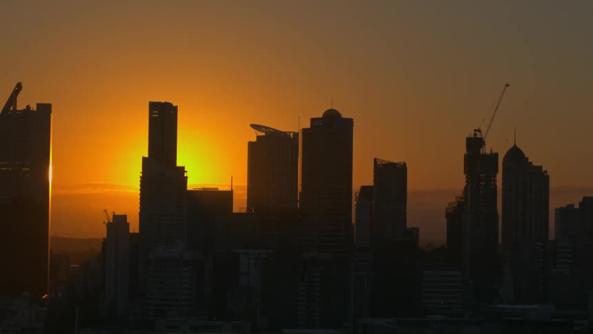 The sun sets behind a city skyline under construction