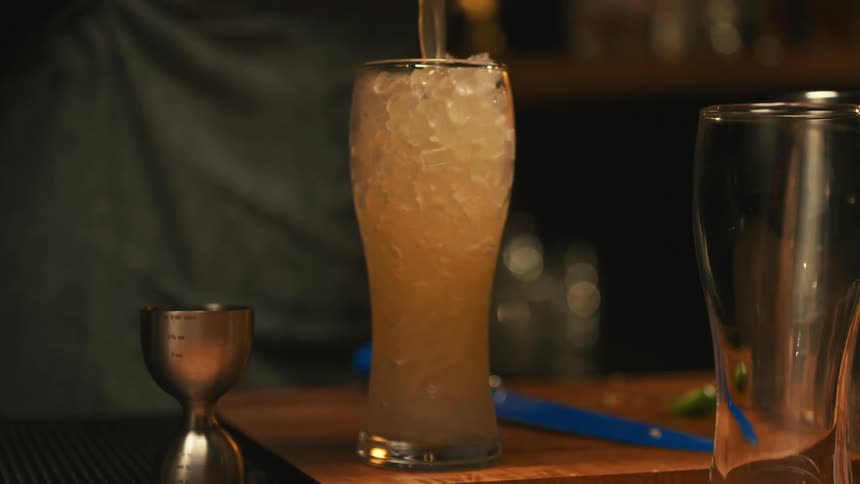 A bartender pours drink over ice in a tall glass