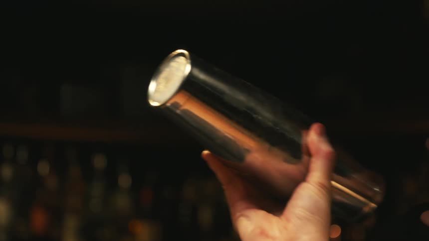 Bartender with tattoo on his fore arm gently shakes cocktail in metal shaker