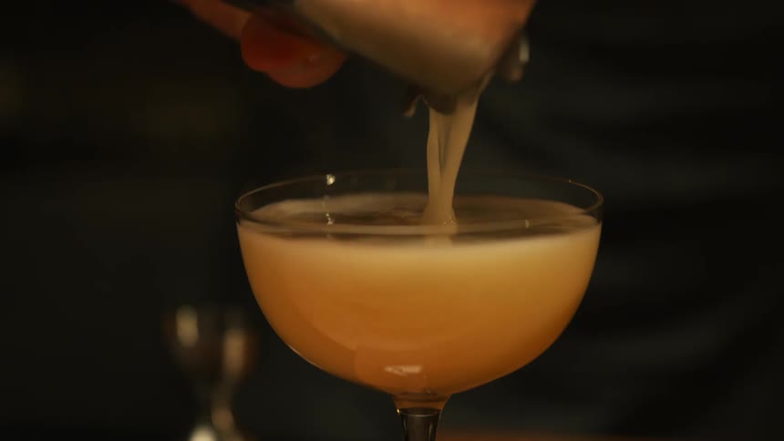 The bartender pours the mixed drink in the glass