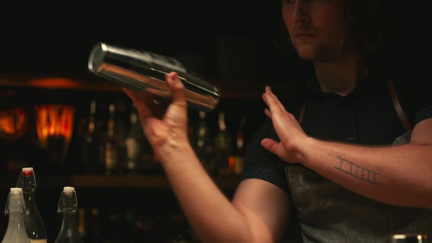 A bartender in a restaurant shakes a shaker as he makes a cocktail