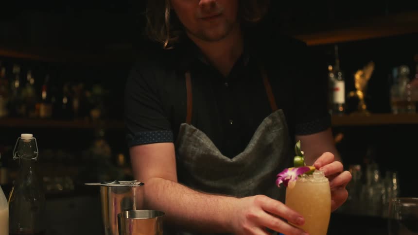 A bartender adds an olive garnish to a cocktail
