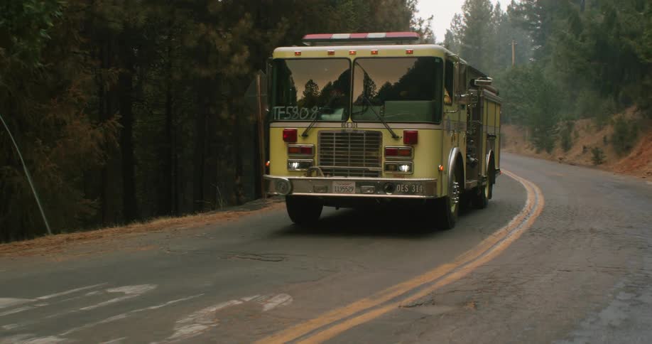 Firetrucks move along road through forest near intersection