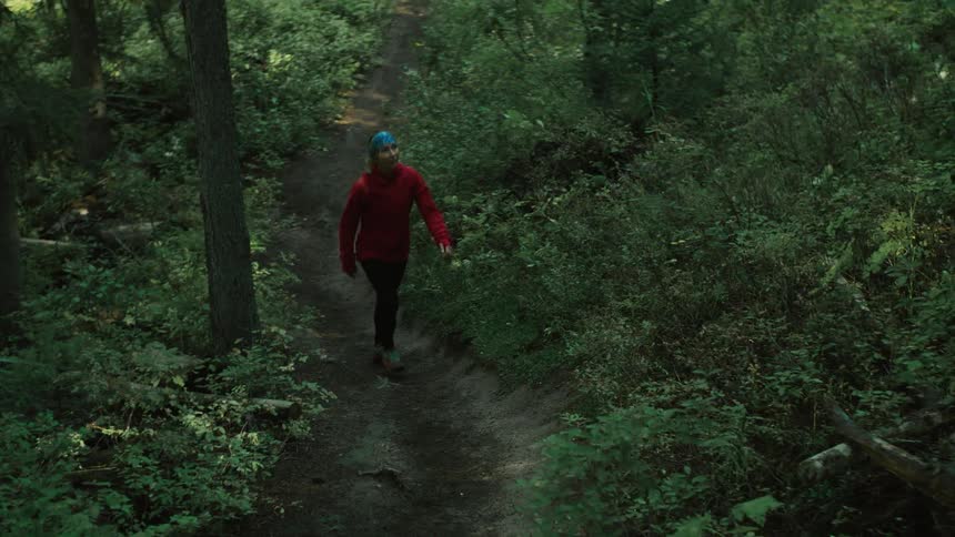 There is a young white woman that is walking on a trail in the forest area