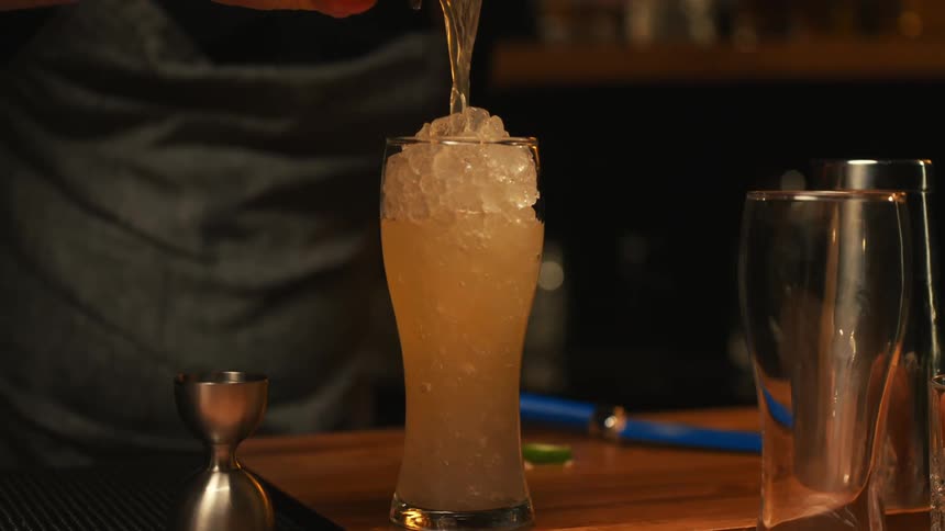 A bartender is pouring a drink into a glass filled with ice from a metal container
