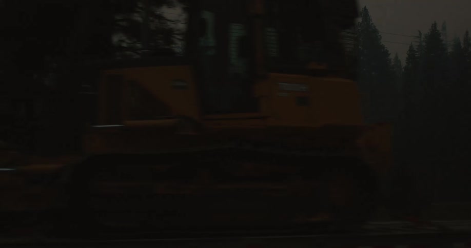 Semi trucks and construction equipment sit parked near field in foggy conifer forest
