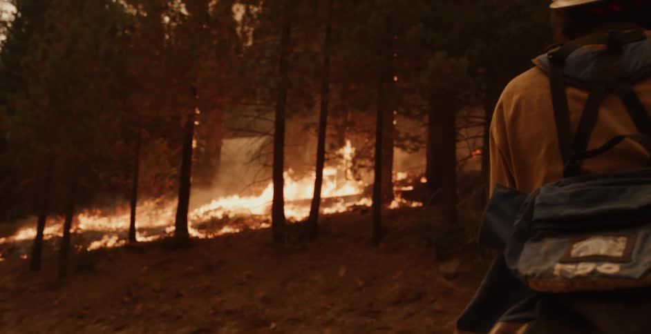 There is a fire going on outdoors with a fireman who is close by